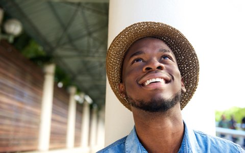 man wearing a hat leaning backwards on a pillar smilling wide
