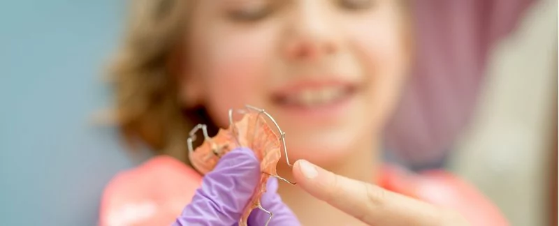 Dental professional holding a retainer in front of a child.