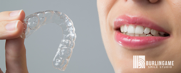 Burlingame smile studio banner of a woman holding Invisalign Clear Aligners