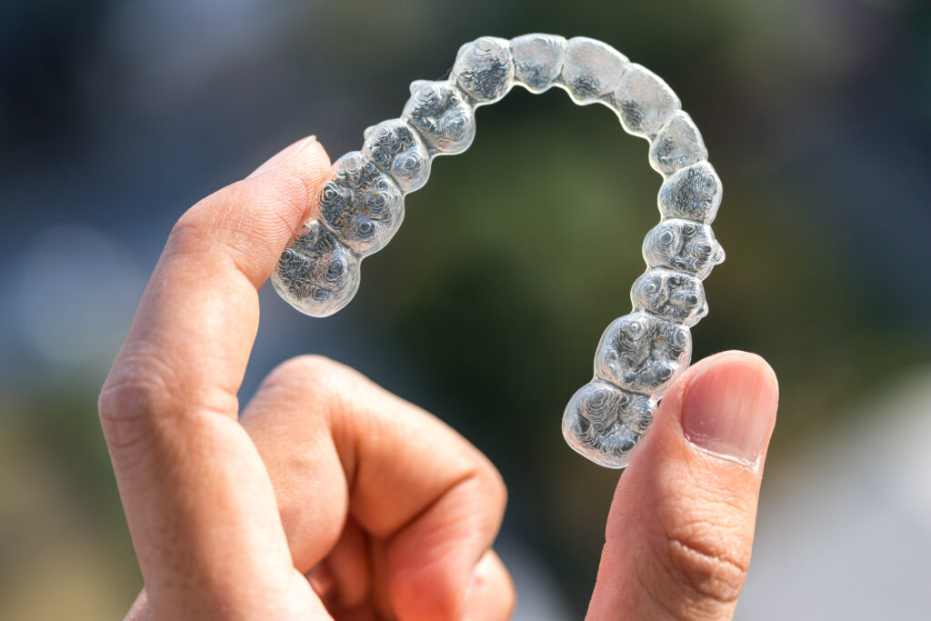 A hand holding a clear dental aligner against a blurred background.